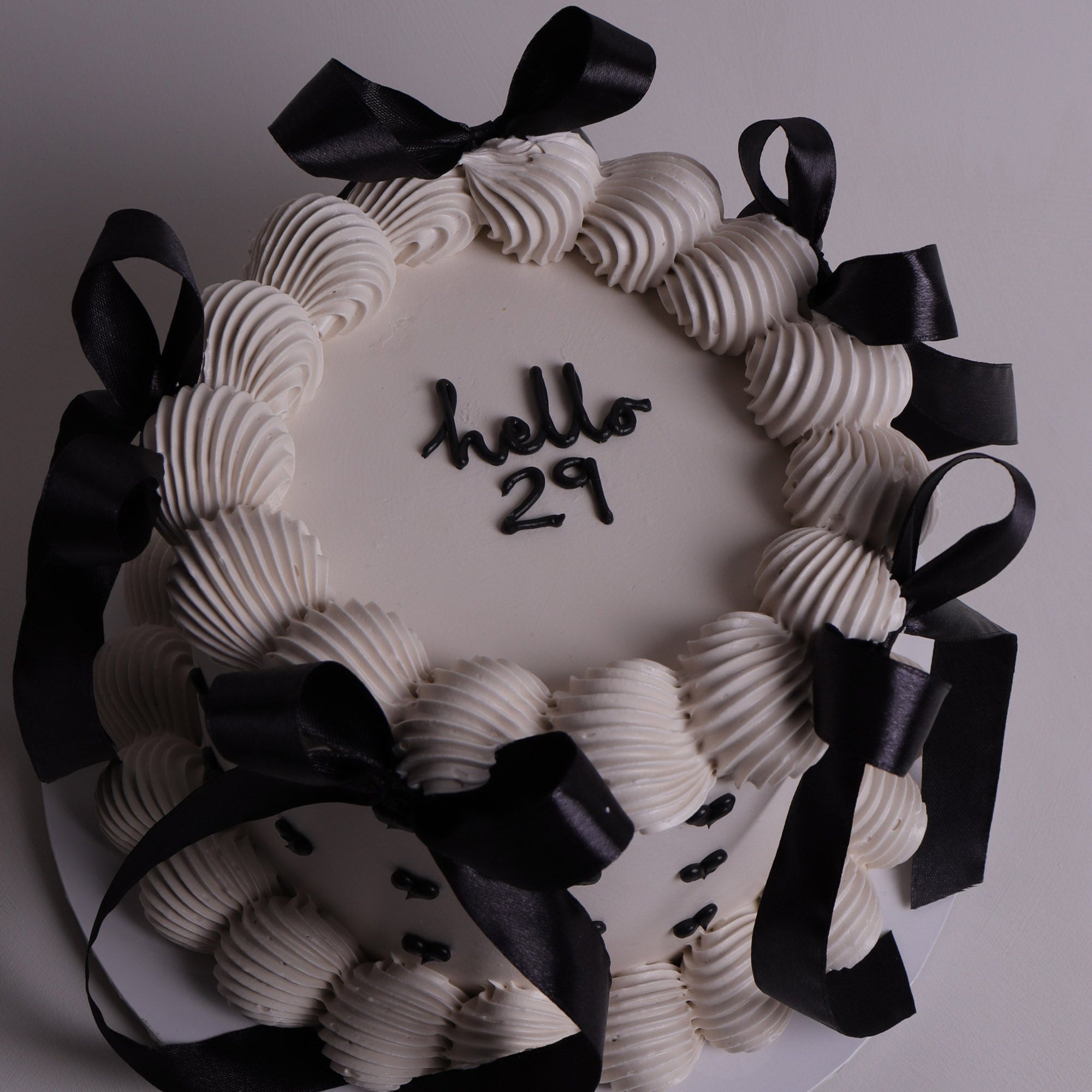 White vintage-style cake with piped buttercream swirls, black ribbon bows and black heart details – elegant celebration cake in Melbourne