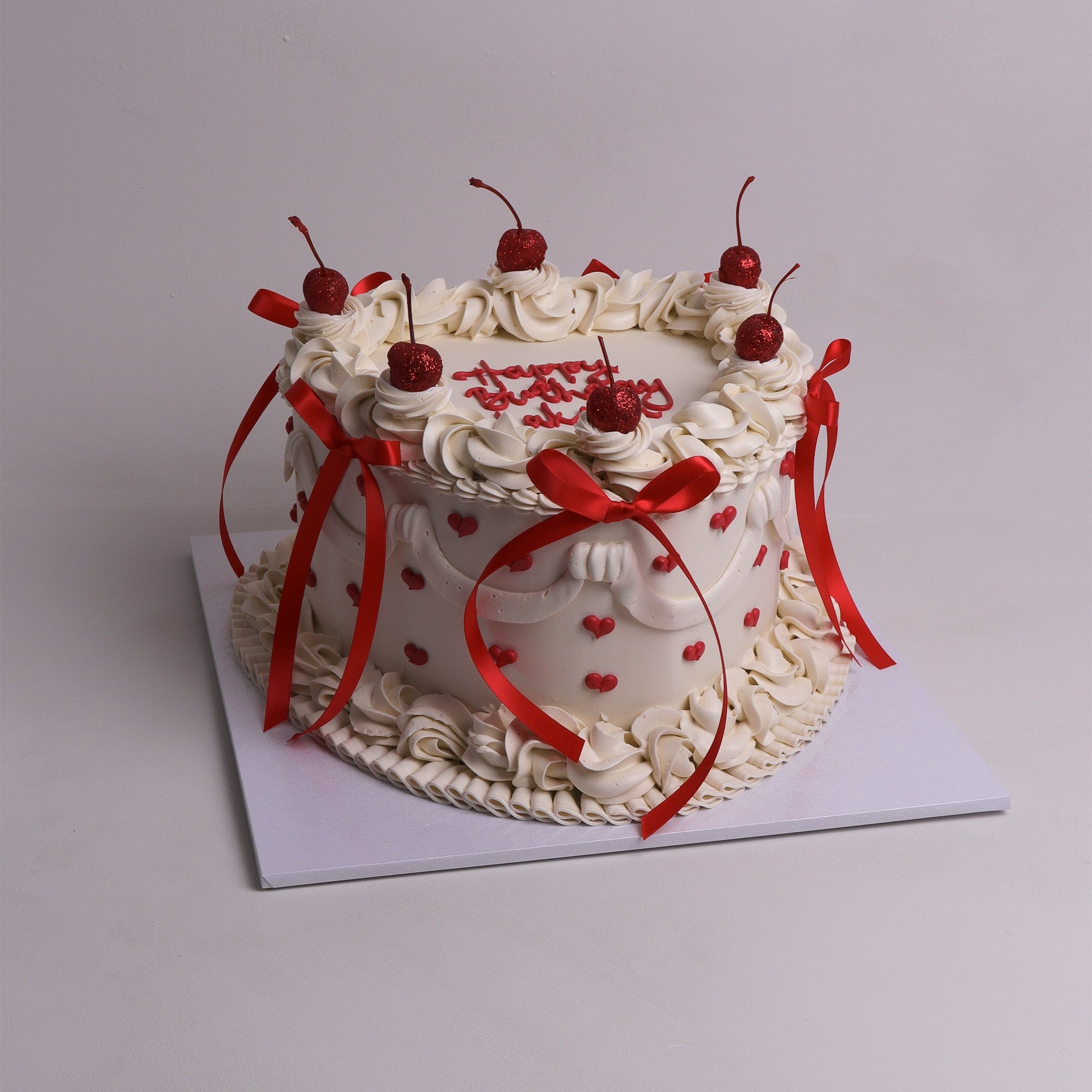 Heart-shaped vintage-inspired cake with red cherries, piped cream swirls and ribbon details – celebration cake in Melbourne