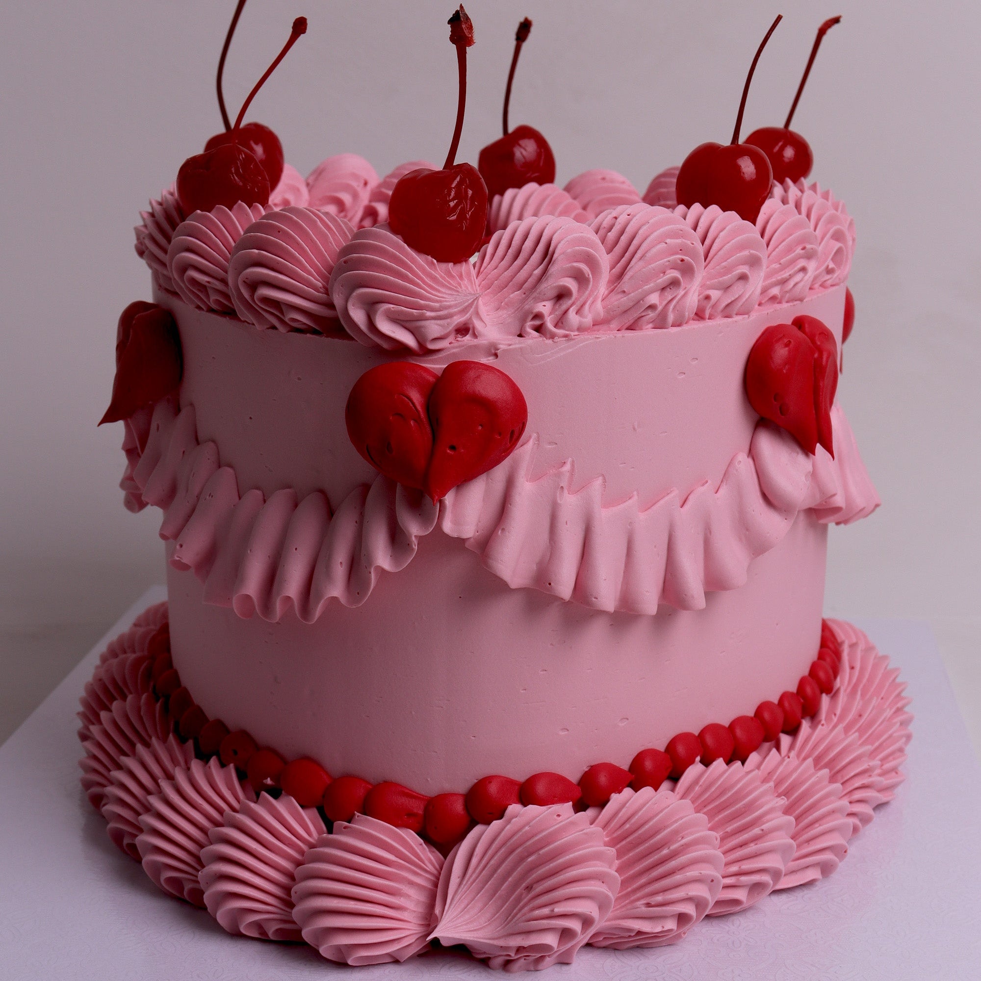 heart cake in shades of pink with ruffled buttercream borders, maraschino cherries and bold white lettering – perfect for hens parties, birthdays and romantic celebrations