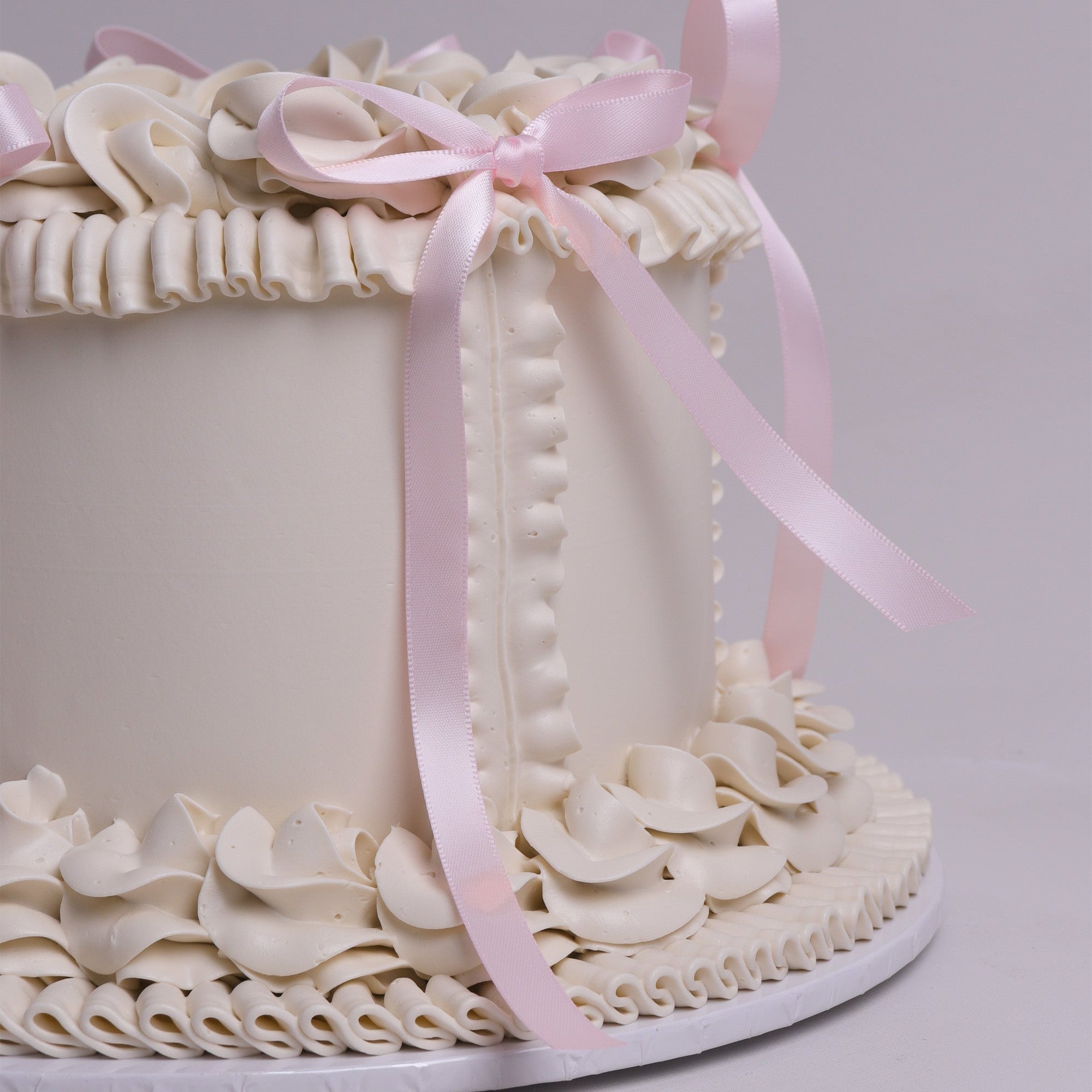 Elegant round vintage buttercream cake decorated with piped swirls, pastel pink bows and classic retro detailing – perfect for baby showers, birthdays and special events