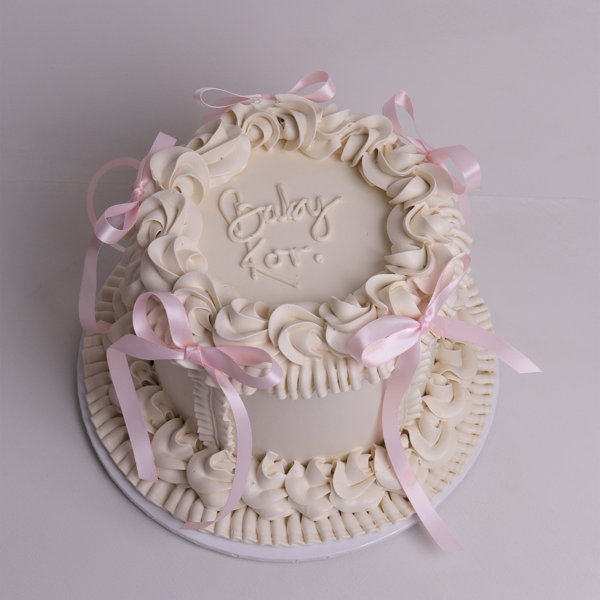 White vintage-style celebration cake with piped buttercream swirls and soft pink ribbon bows – baby shower cake in Melbourne