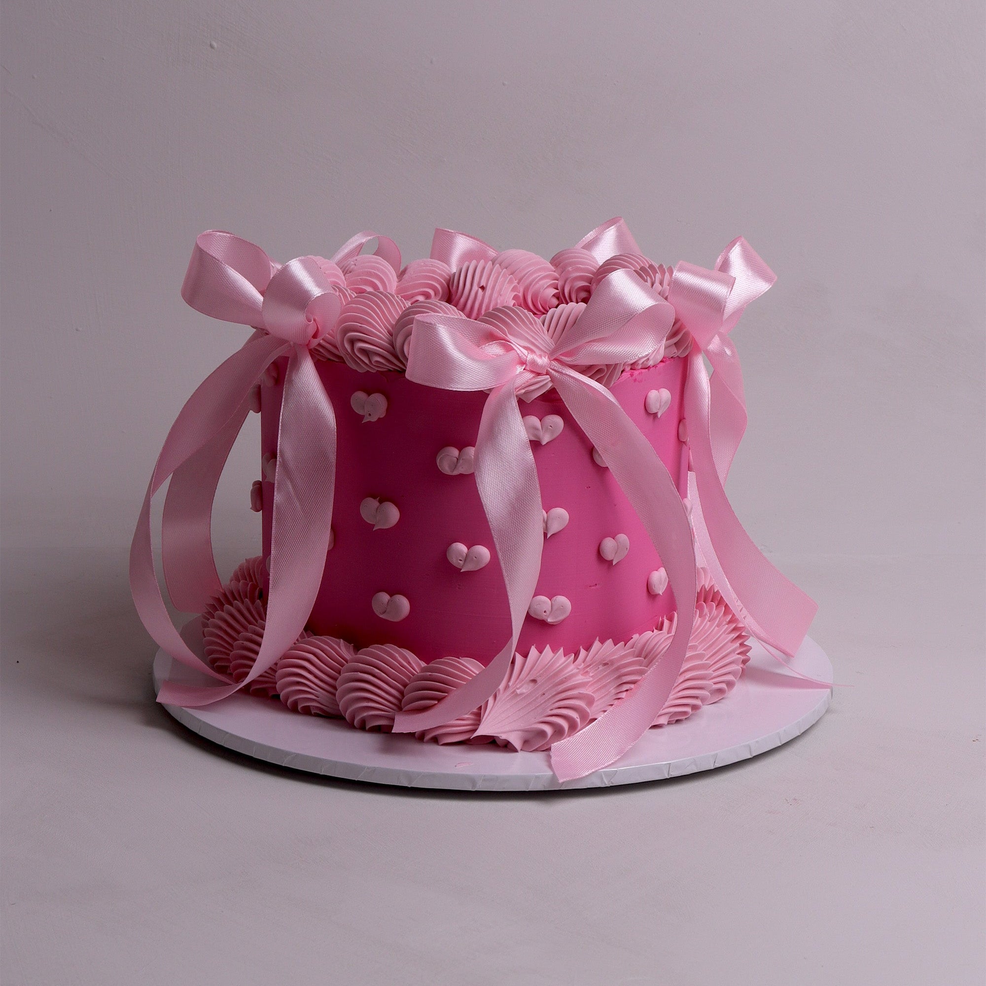 Round retro pink cake decorated with piped buttercream ruffles, pastel pink ribbon bows and mini heart accents.