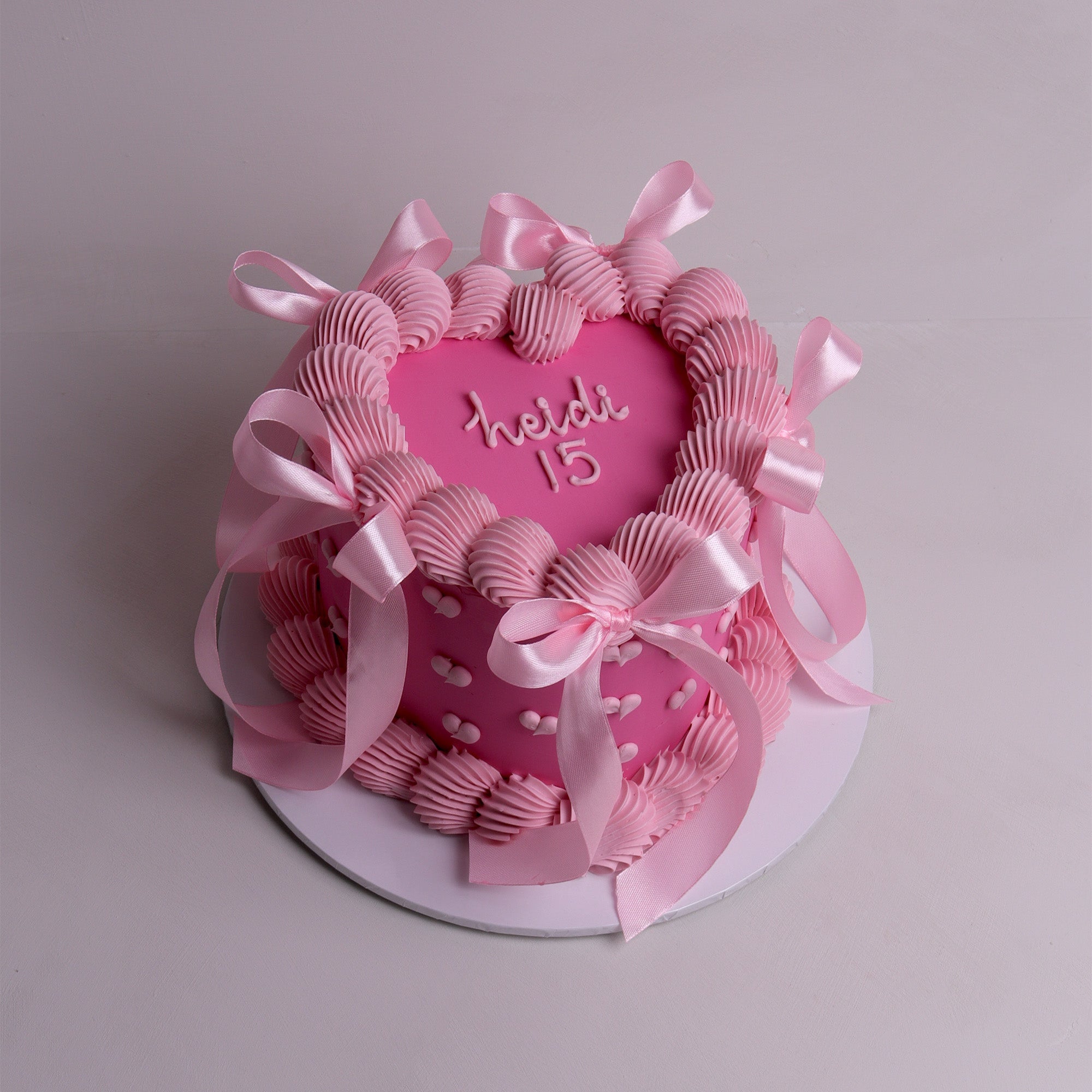 Pink vintage-style birthday cake with piped buttercream swirls, satin ribbon bows and heart details – celebration cake in Melbourne