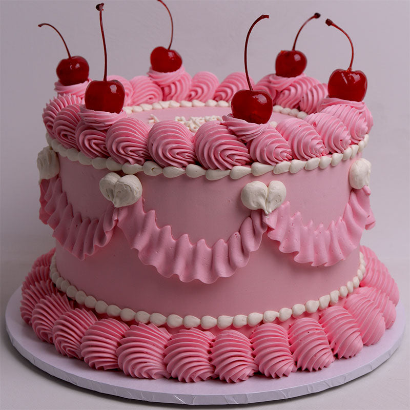 Pink frosted vintage birthday cake with cherry decorations on a light gray background