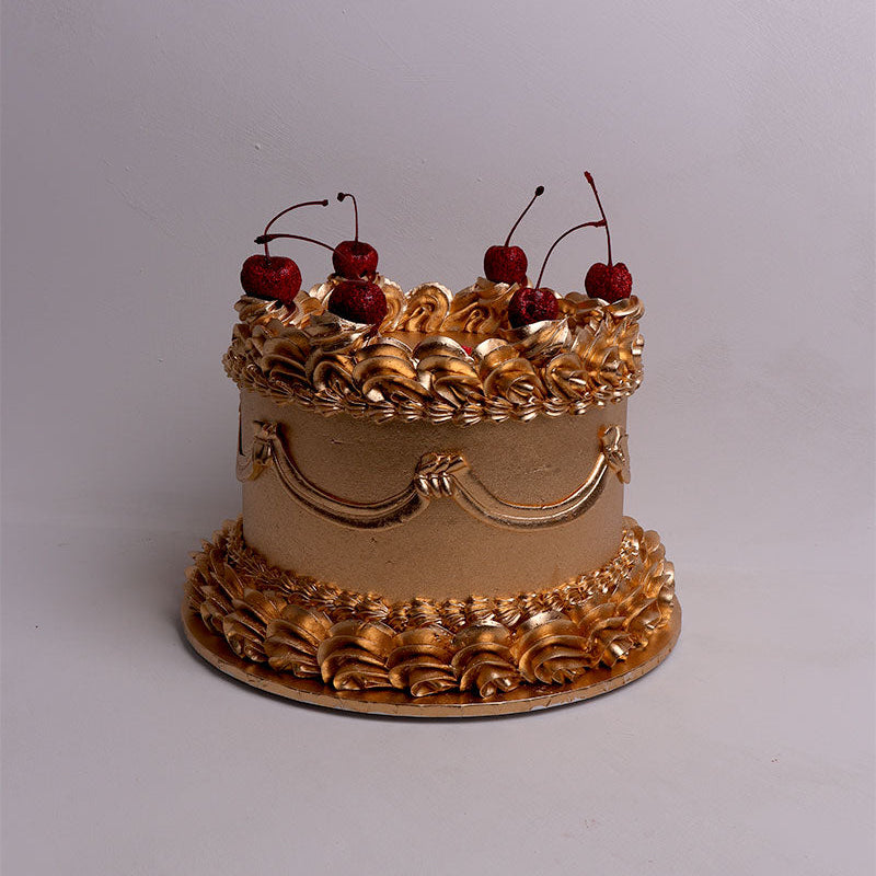 Decorative cake with gold icing and cherries on a plain background