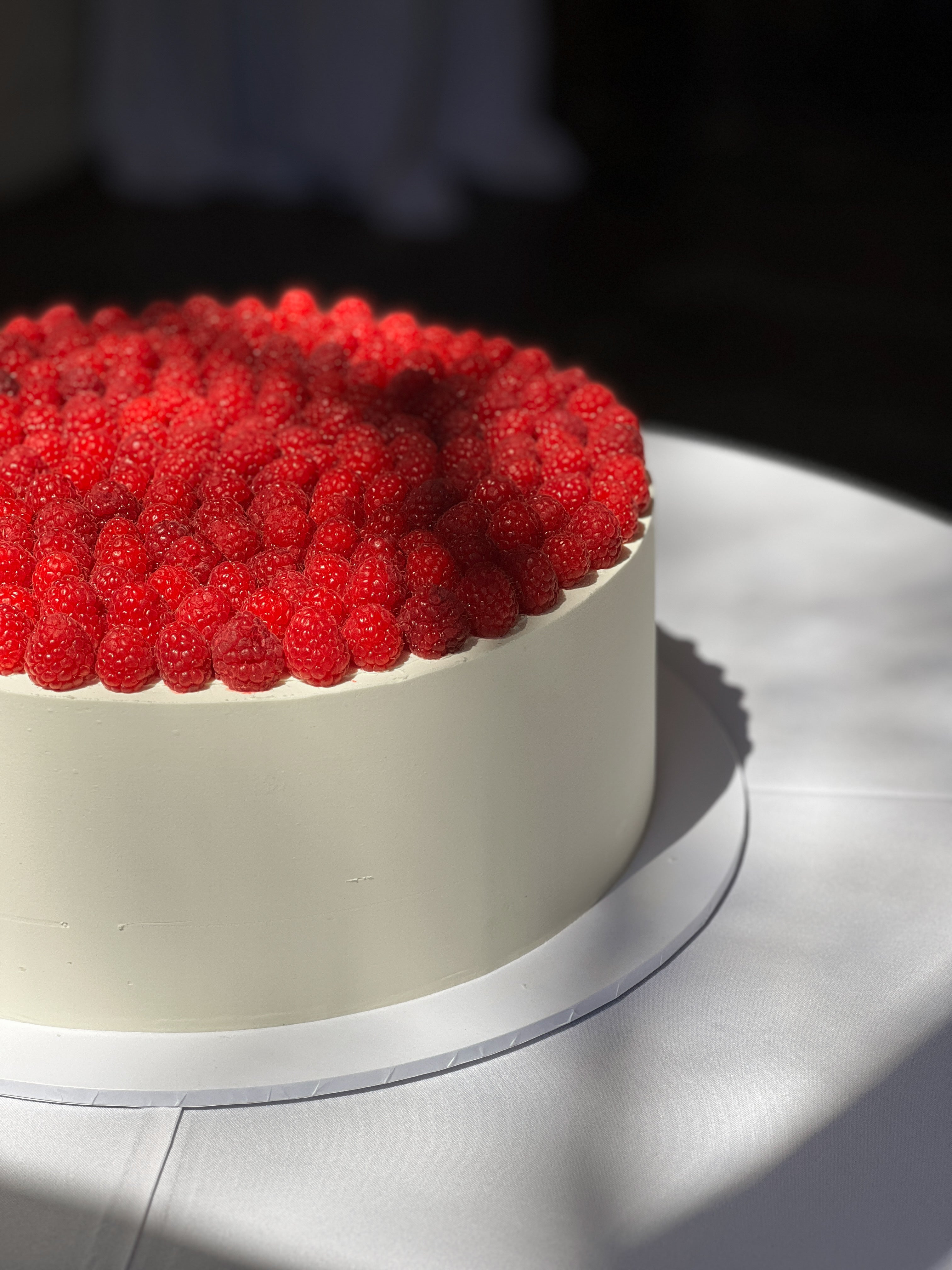 Minimalist white cake topped with fresh raspberries, perfect for a modern wedding or special occasion.