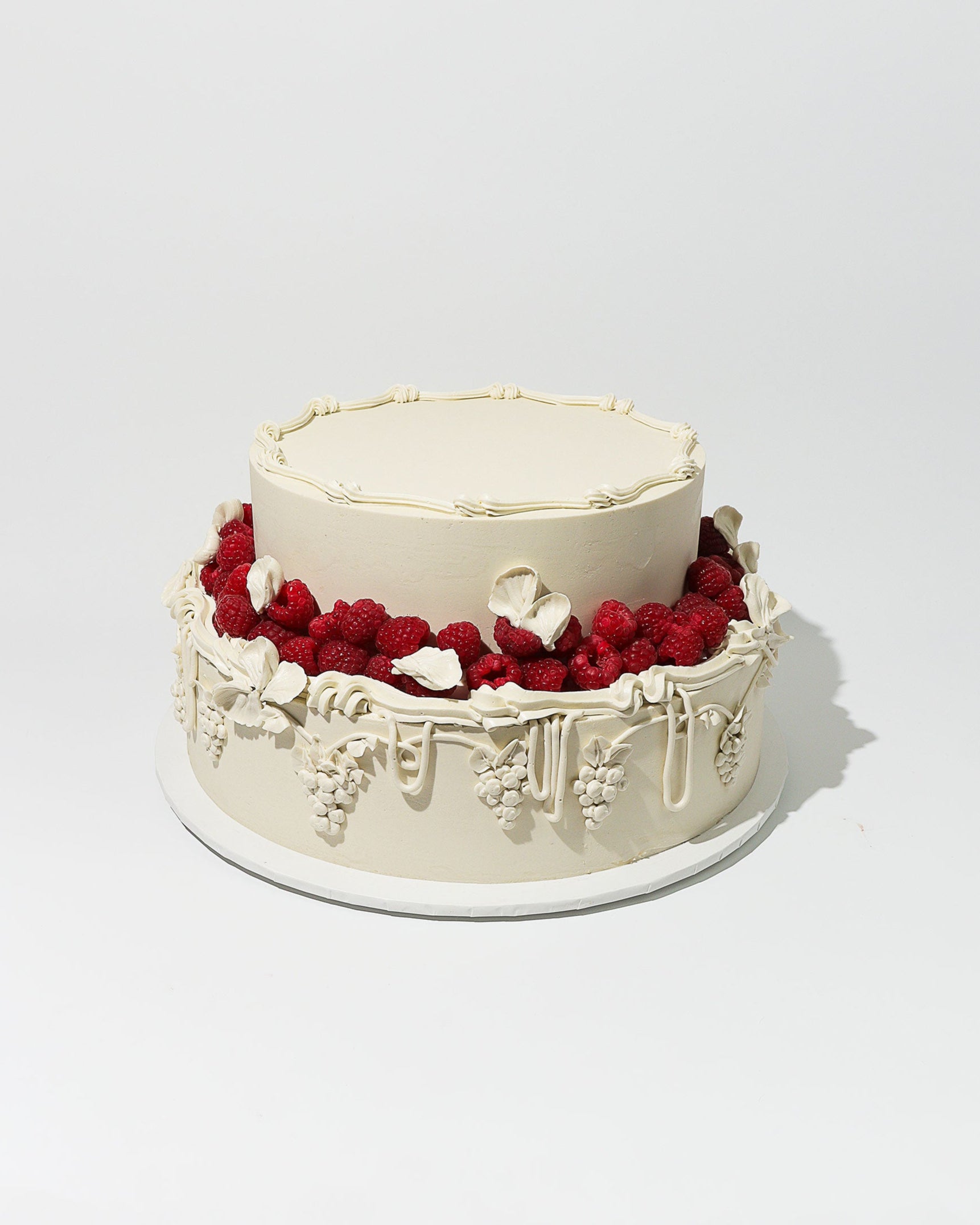 Wedding cake with white frosting, red berries, and white flowers on a light gray background