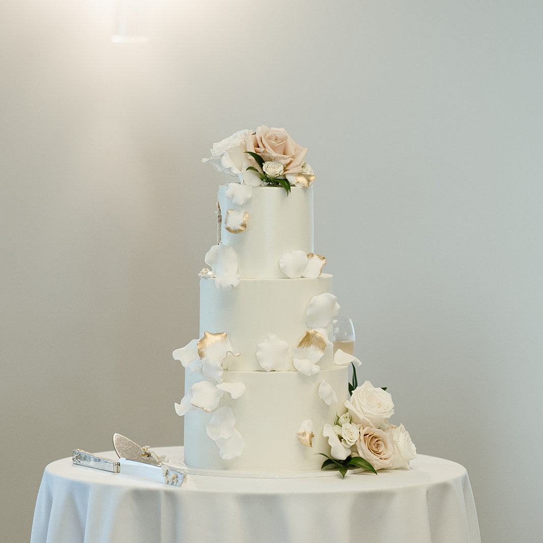 Three-tiered wedding cake with floral decorations on a white tablecloth against a plain background